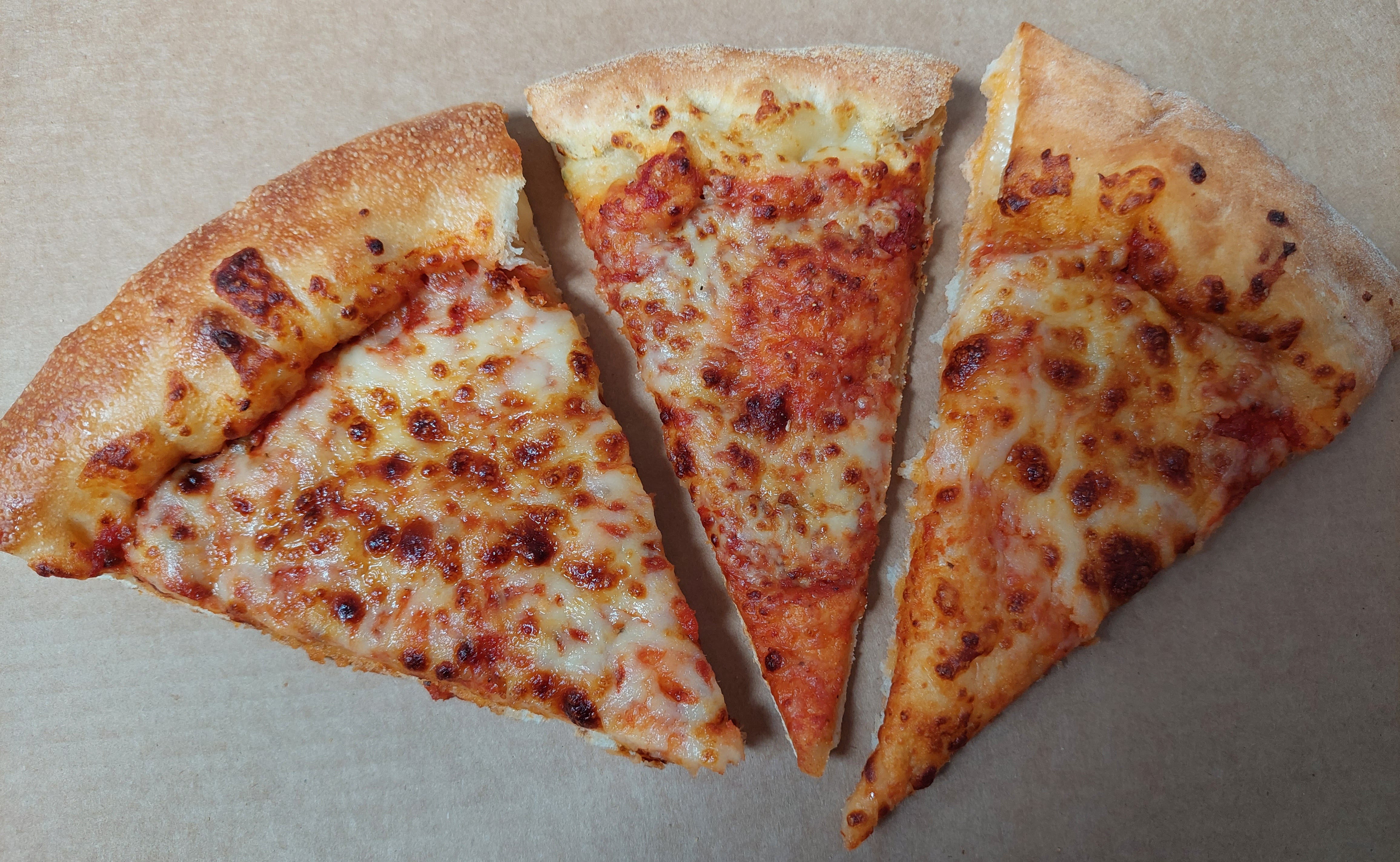 Pizzastücke von Pizza Hut, Domino's und Papa John's nebeneinander in einer Pizzaschachtel