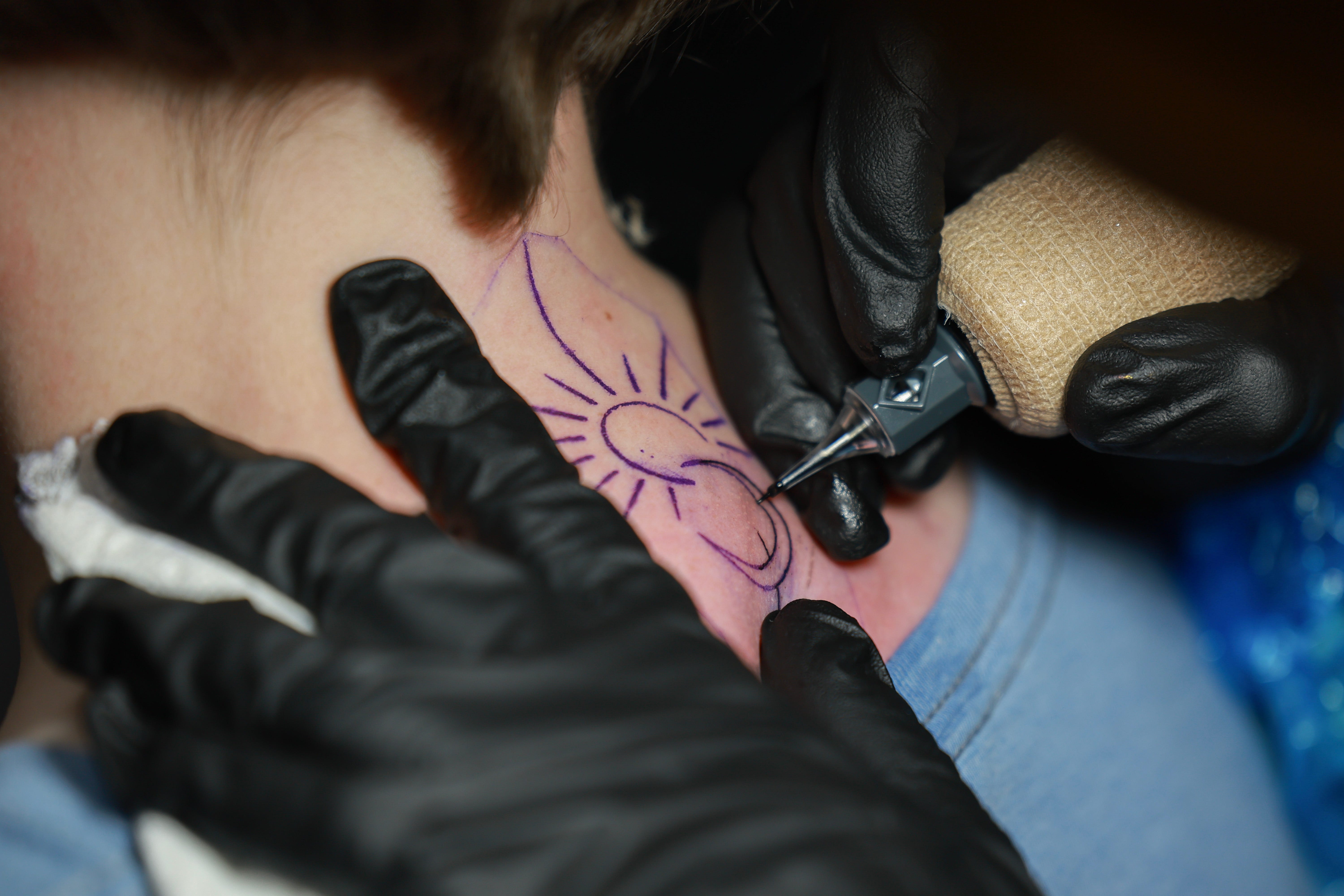 Dawn MacDonald, die Besitzerin von Crowe's Tattoos, platziert am 7. April 2024 in Houlton, Maine, ein Sonnenfinsternis-Tattoo auf dem Hals von Alayna Acott.  MacDonald sagte, sie habe einen stetigen Strom von Kunden, die sich Sonnenfinsternis-Tattoos wünschen.