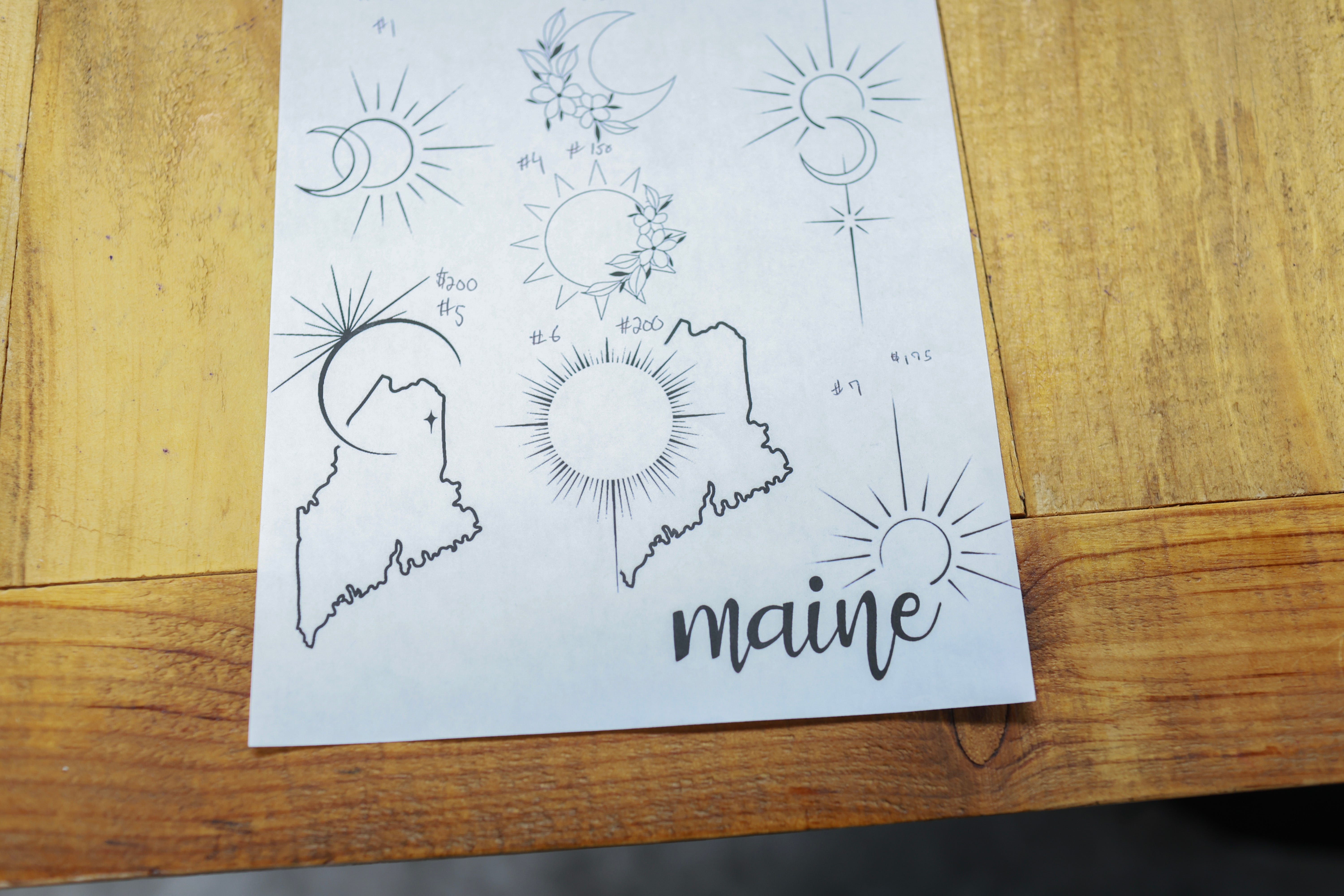 Eclipse-Tattoo-Designs werden am 7. April 2024 bei Crowe's Tattoos in Houlton, Maine, ausgestellt.  Dawn MacDonald, die Besitzerin des Ladens, sagte, sie habe einen stetigen Strom von Kunden, die sich Sonnenfinsternis-Tattoos wünschen.  Millionen von Menschen strömten in Gebiete in ganz Nordamerika, die sich auf dem „Weg der Totalität“ befinden, um eine totale Sonnenfinsternis zu erleben.