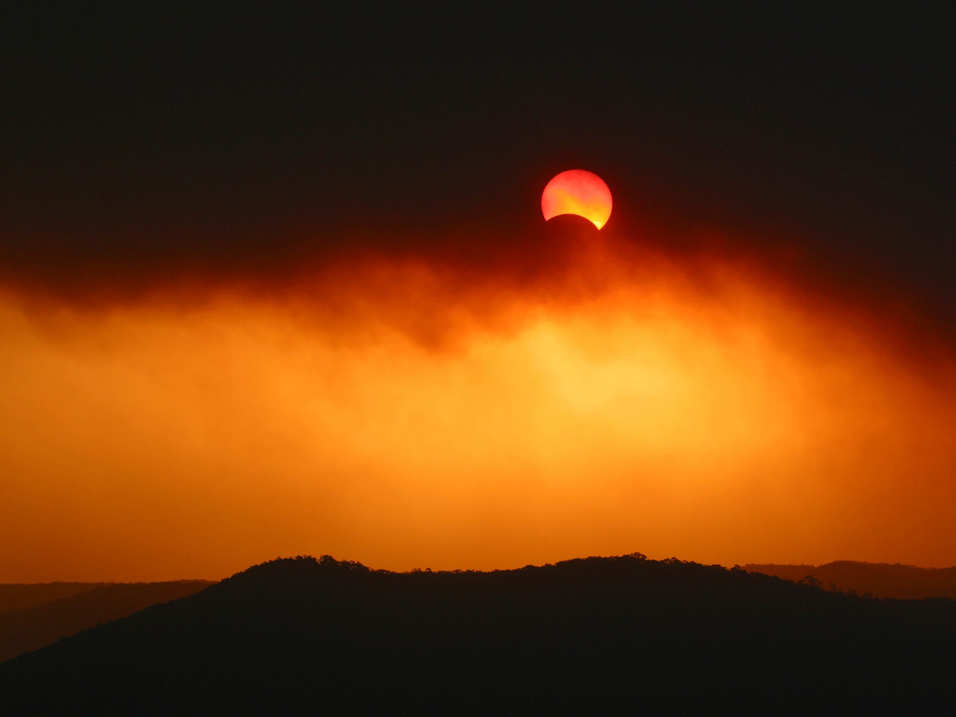 Eine partielle Sonnenfinsternis erscheint feuerrot durch dichte Buschfeuerrauchwolken.