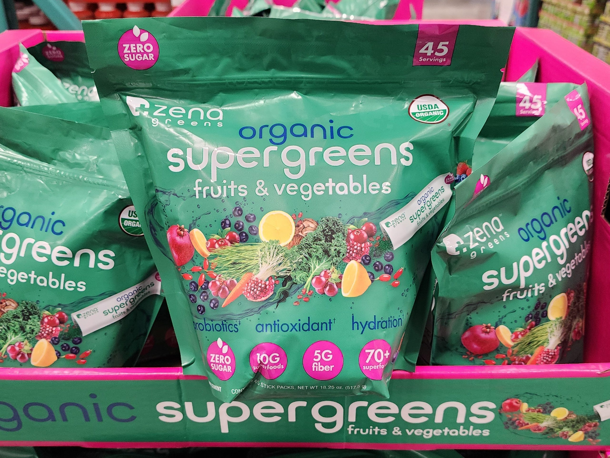 Grüne Beutel mit Bio-Supergreens-Obst und -Gemüse von Zena Green mit Abbildungen von Karotten, Zitronen, Beeren und anderen Lebensmitteln auf der Verpackung