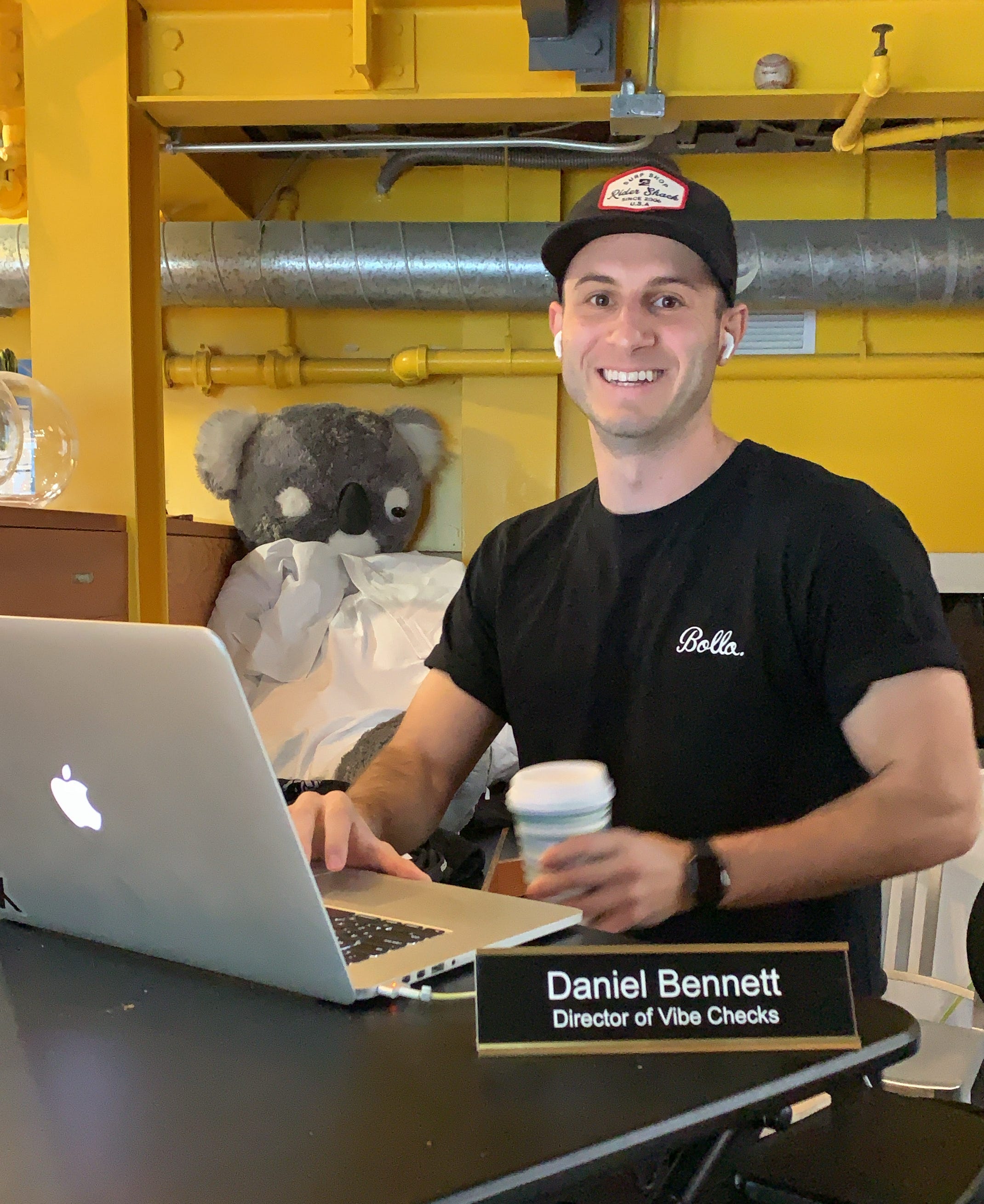 Daniel Bennett lächelt in die Kamera.  Vor ihm hängt ein Namensschild mit der Aufschrift „Daniel Bennett, Director of Vibe Checks“.