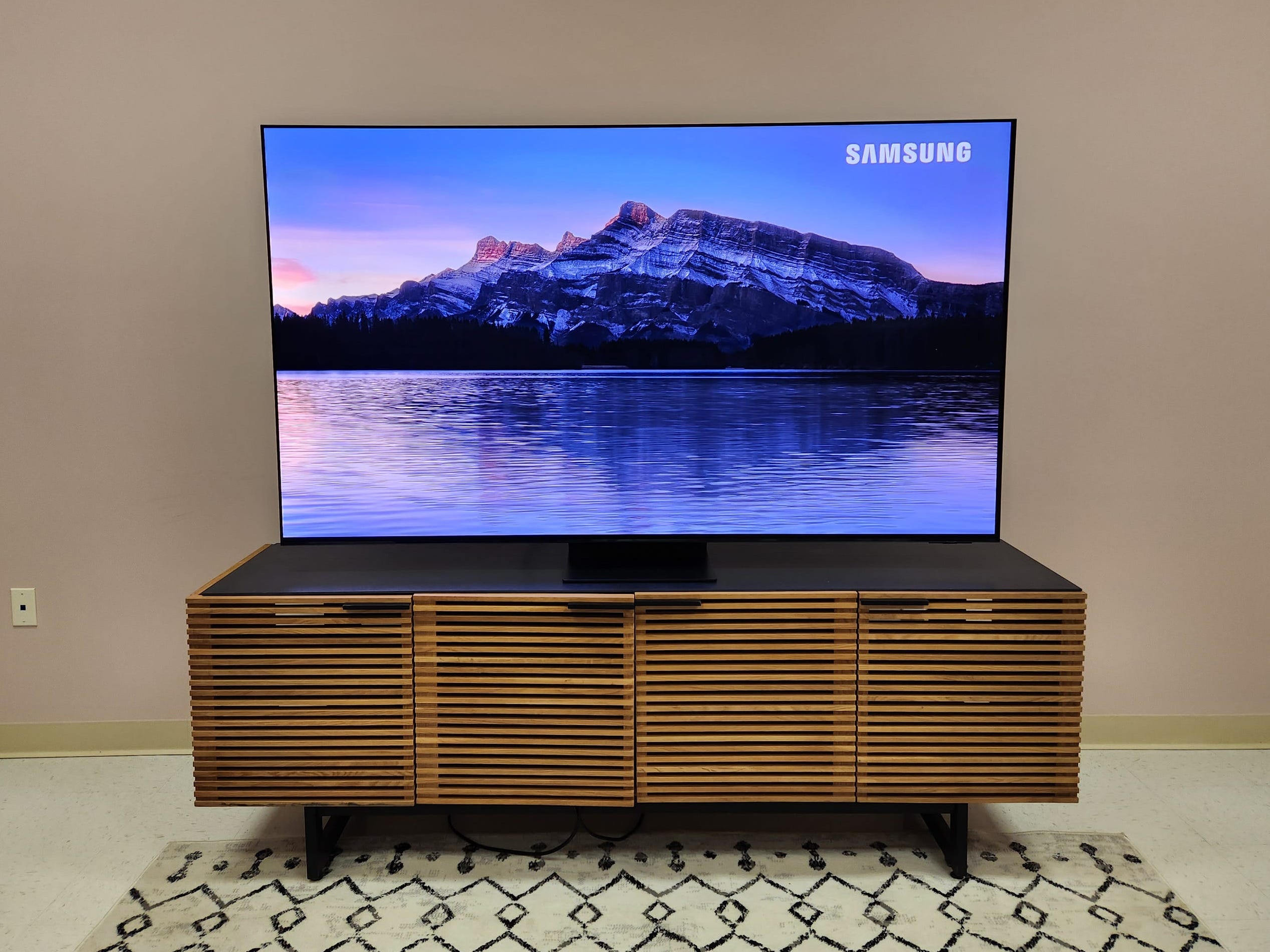 Eine Sequenz mit einer Bergkette mit Blick auf einen See, angezeigt auf einem Samsung S95C OLED-Fernseher, der auf einem Unterhaltungsständer steht.