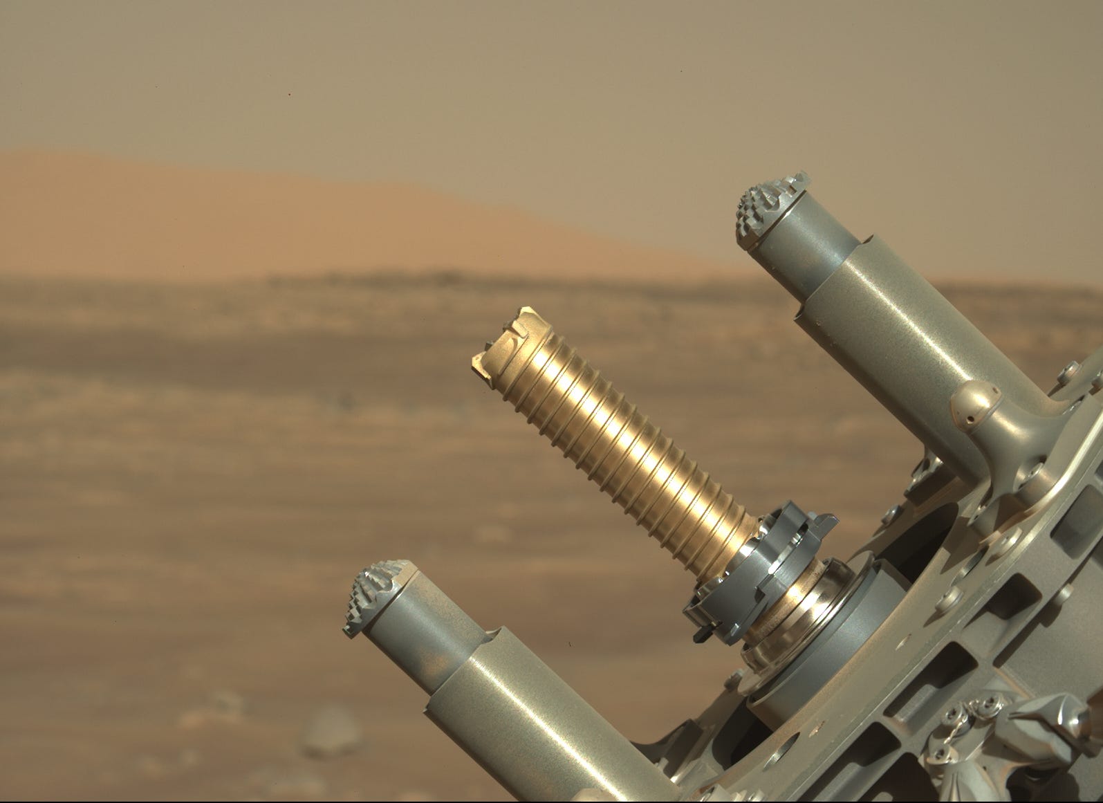 Der Roboterarm des Perseverance Rover hält ein goldenes Rohr zum Entkernen von Proben vor dem Hintergrund der Marsebene hoch