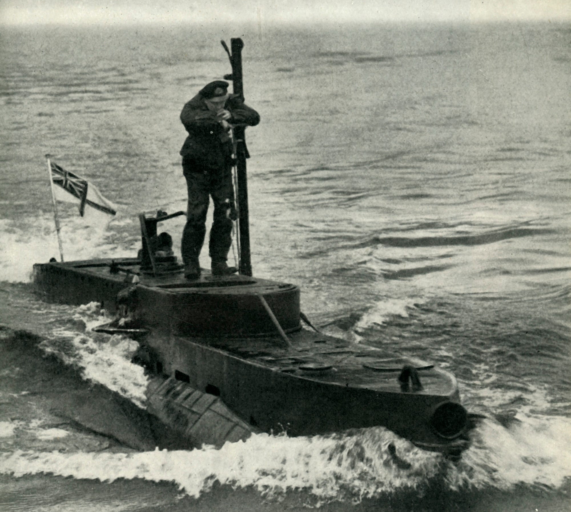 Eine Person in Armeeuniform steht auf einem kleinen U-Boot mit einer britischen Flagge darauf