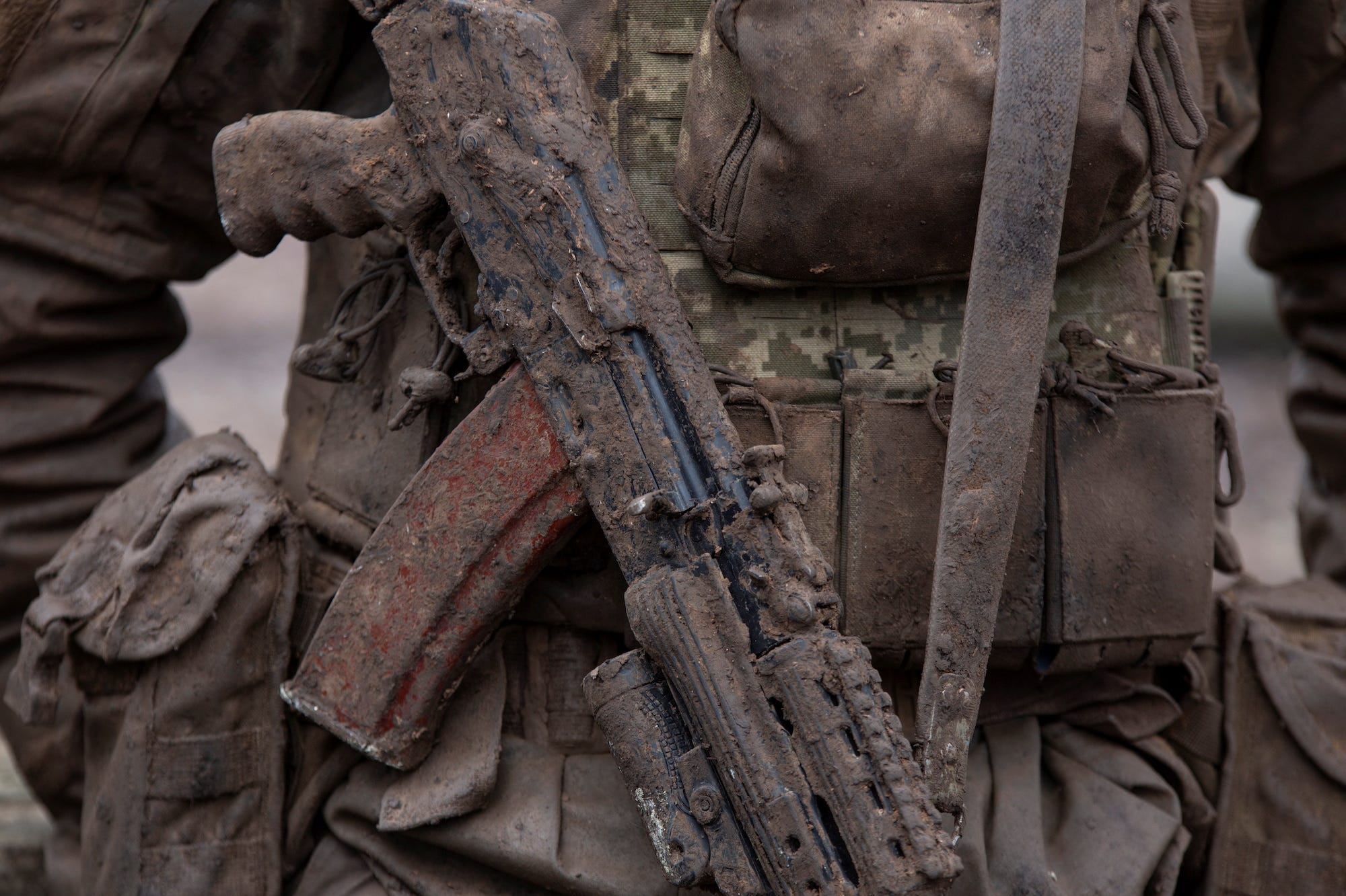 Eine mit Schlamm bedeckte AK-74 um den Hals eines ukrainischen Soldaten in Tarnkleidung
