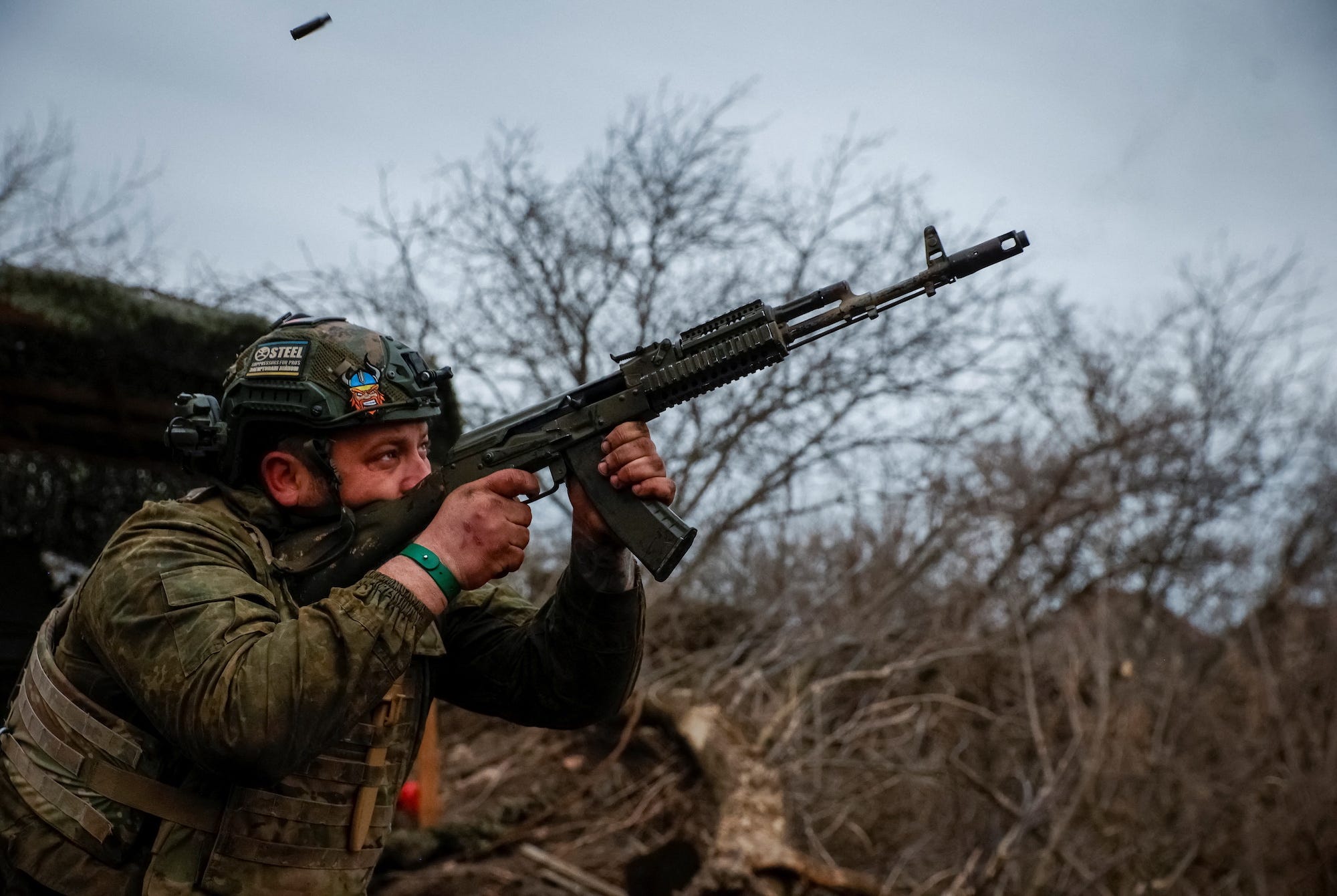 Ein ukrainischer Soldat in Tarnkleidung feuert mit kahlen Bäumen und einem grauen Himmel im Rücken eine AK-74 ab