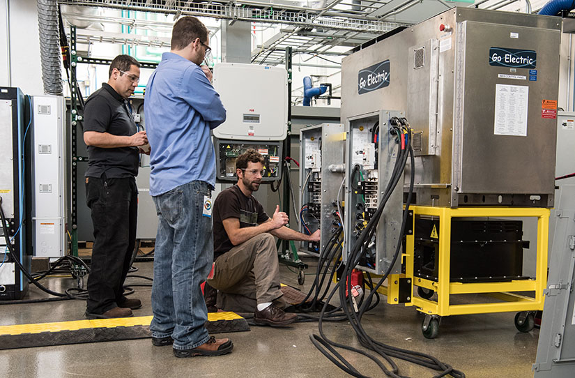 Drei Ingenieure arbeiten in einem Labor an einem Go Electric-Wechselrichter. 