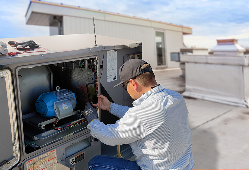 Ein Mann installiert einen blauen Motor in einer HVAC-Einheit auf dem Dach eines Gebäudes.