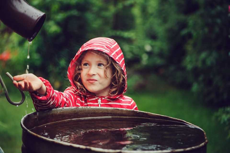 Sustainable garden: child in front of a full rain barrel
