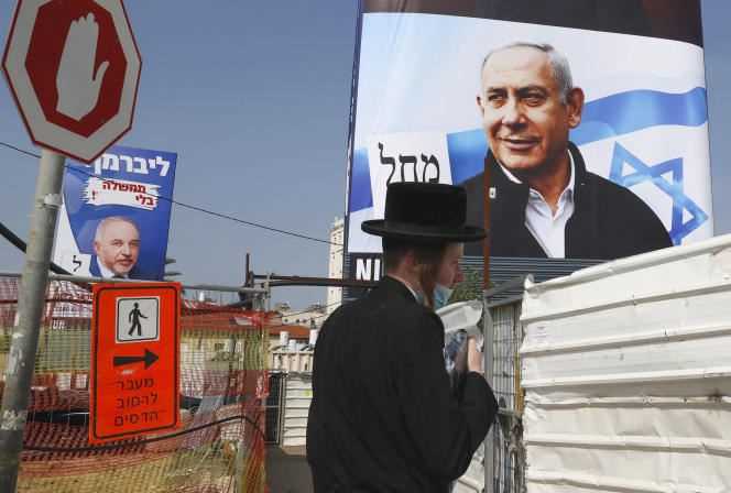 An ultra-Orthodox Jew walks past roadworks with campaign posters from Avigdor Lieberman, leader of the Israel Beitenu party, and Benjamin Netanyahu, from Likud.  In Bnei Brak, Israel, March 14, 2021.