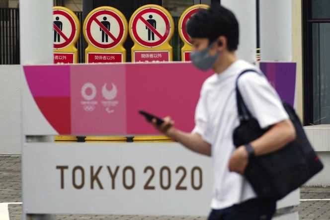 A man wearing a mask walks past a poster for the Tokyo Olympics, May 11, 2021.