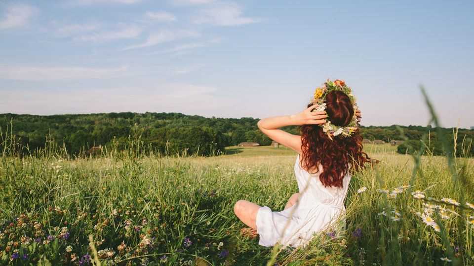 Make a wreath of flowers yourself: Woman is sitting in a meadow and wears a wreath of flowers