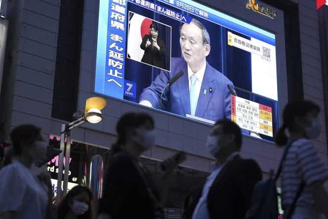 People walk past a big screen as Japanese Prime Minister Yoshihide Suga speaks about the country's health situation in Tokyo on June 17, 2021.