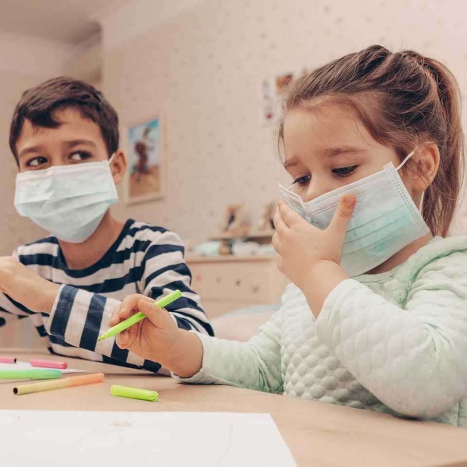 Two children while painting with medical masks.