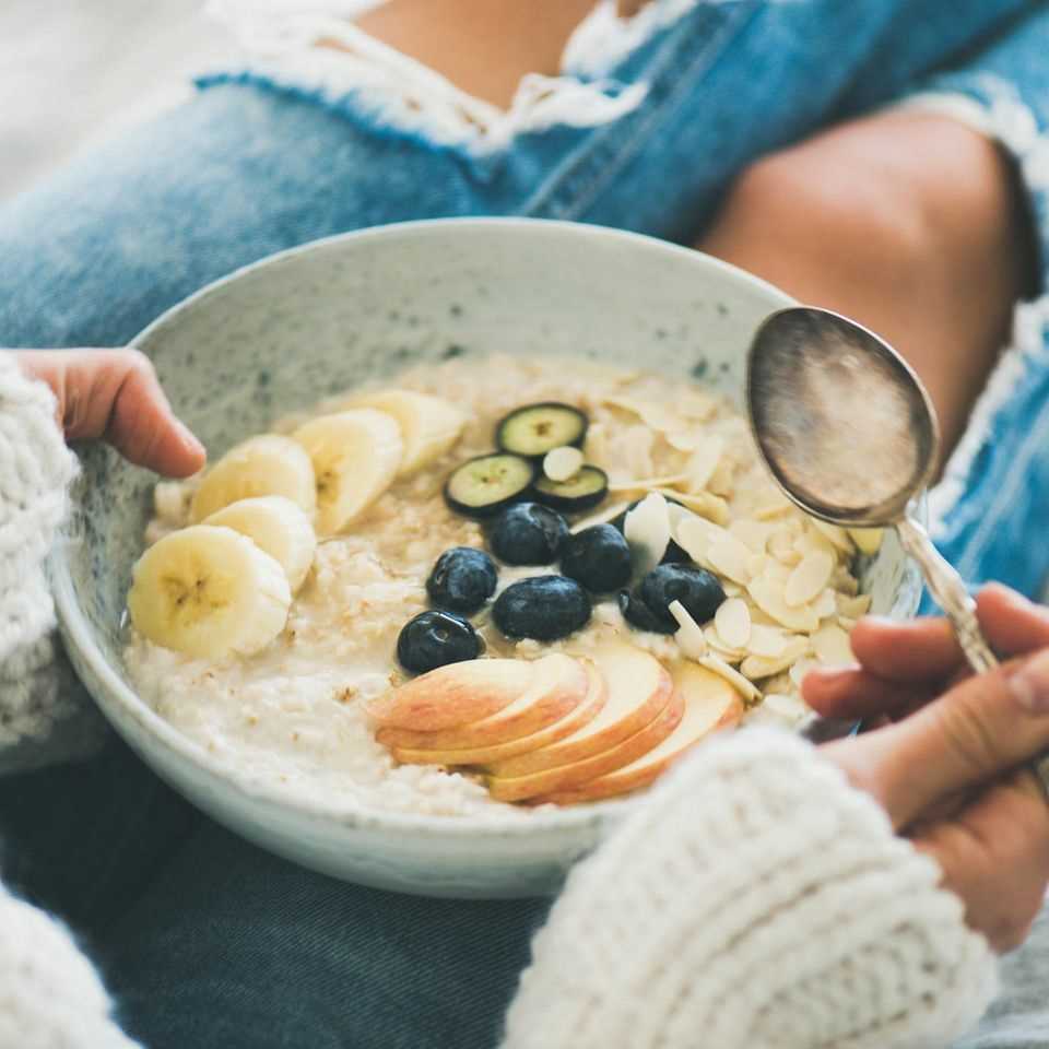 Hot breakfast: woman holds bowl of porridge with fruit on her lap.
