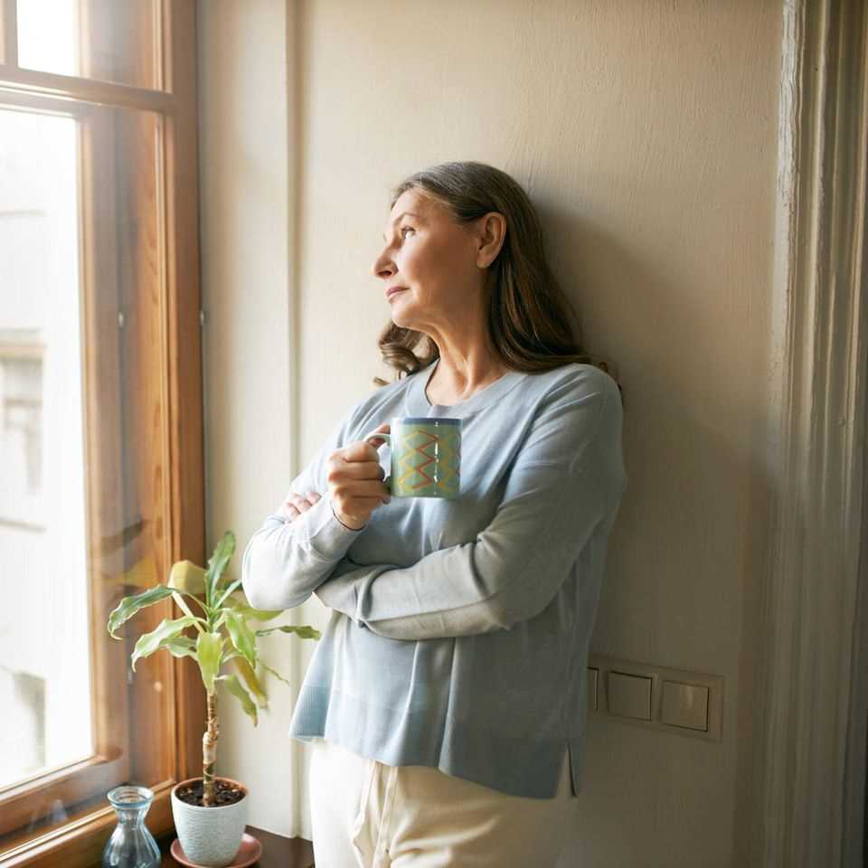 These 6 foods can make menopause worse: A woman looks out the window with a mug in her hand.