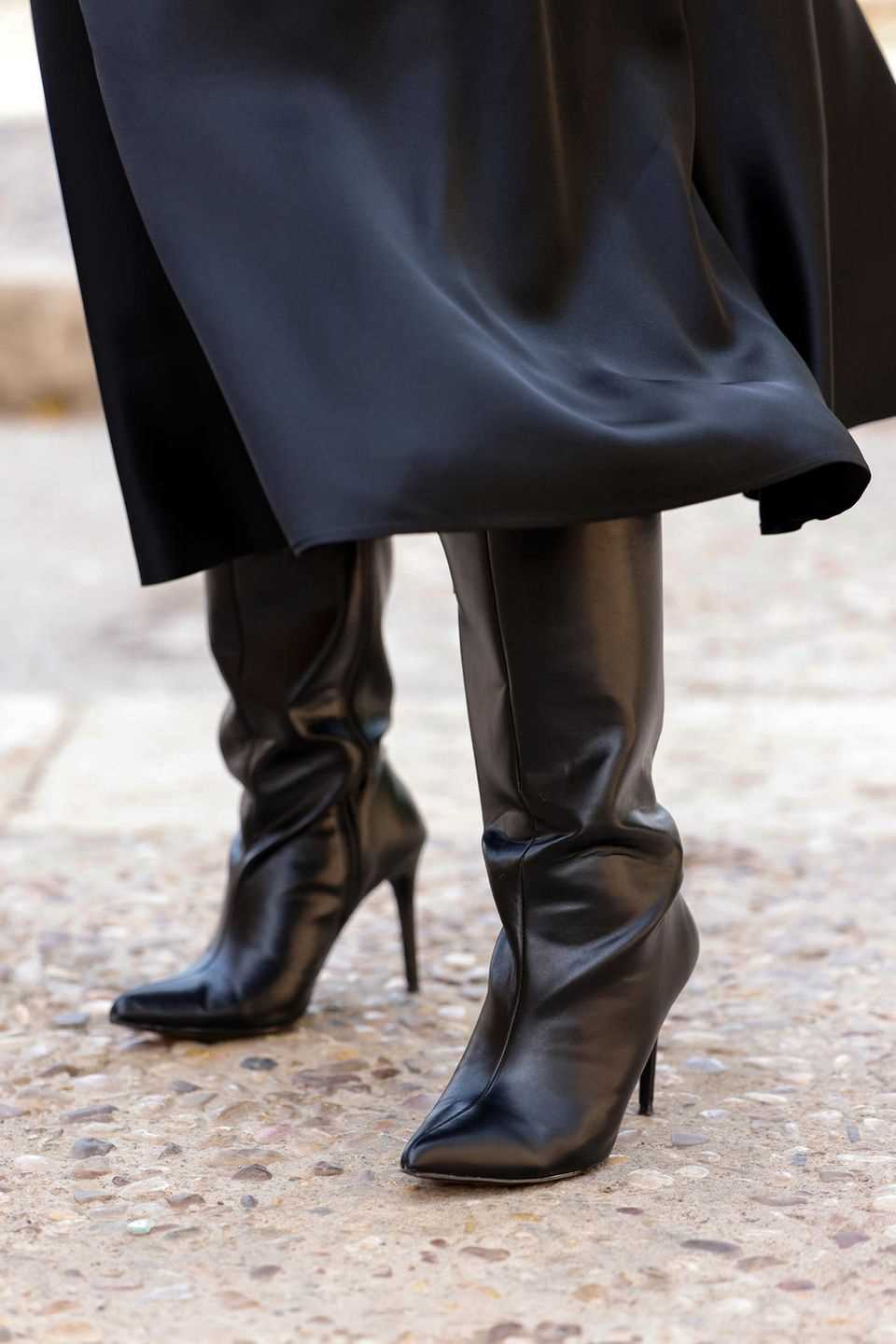 A woman wears black over-the-knee boots and a black skirt