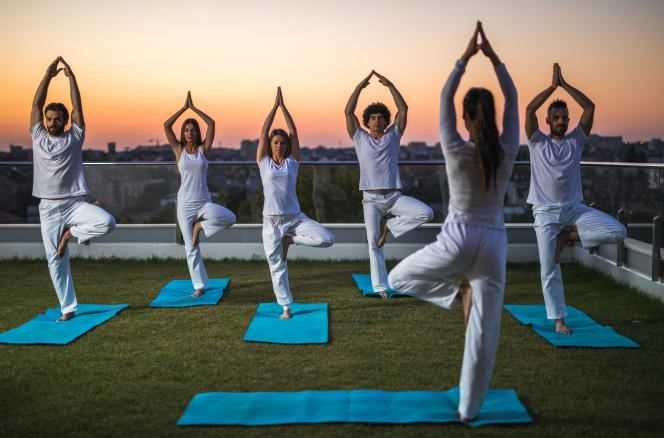 Group of people in the tree pose with a yoga teacher, on a terrace at sunrise.
