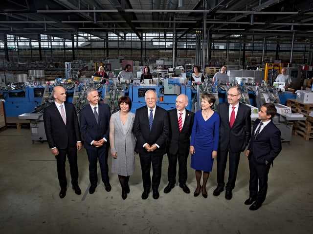 The members of the Federal Council stand in a factory hall.