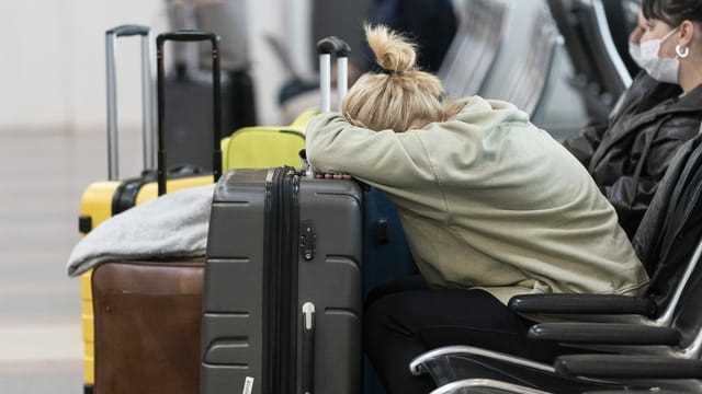 Eine Passagierin schläft mit dem Kopf auf ihrem Koffer.