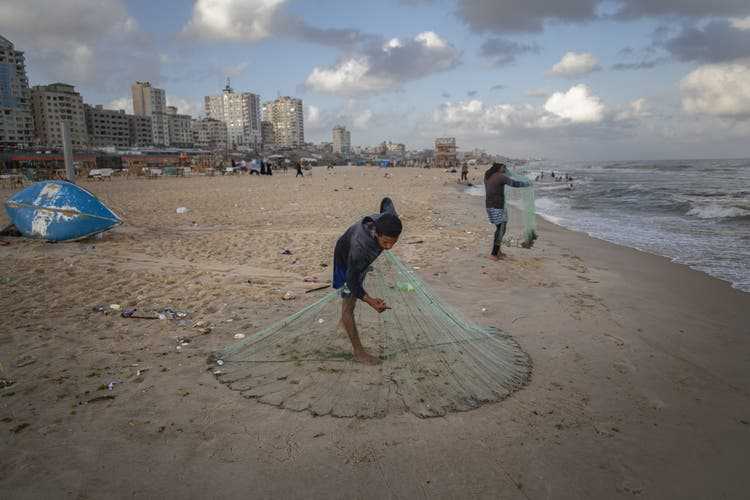 Two young men prepare their fishing nets on the beach in Gaza City.
