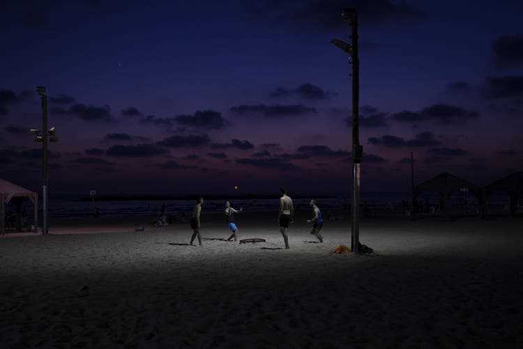 Young Israelis play under a light pole on the beach in the evening. 