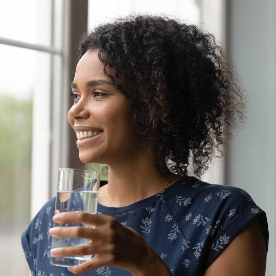 Woman drinking water by the window: 5 reasons why you should drink a glass of water first thing in the morning