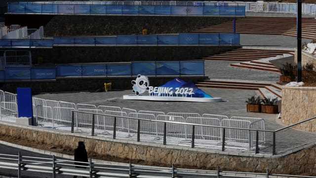 Sicherheitspersonal bewacht ein leeres Gelände auf dem der Schriftzug der Olympischen Spiele ist.