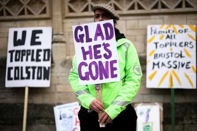 On December 13, 2021, a protester held a 'Glad he's gone' sign outside Bristol Crown Court, where the trial of four people accused of unburning the statue of Edward Colston was being held.