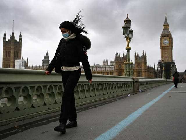 A woman with windblown hair walks across a bridge.