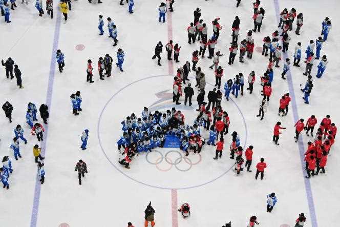 Volunteers who worked at the Olympics take a picture on the ice rink of the Beijing Sports Center after the final of the ice hockey tournament on February 20, 2022.