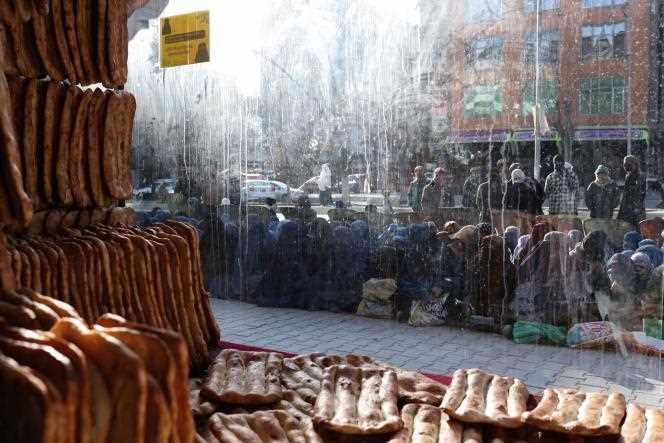 Afghans sit on the ground outside a bakery waiting to receive a ration of bread, in Kabul on January 31, 2022.