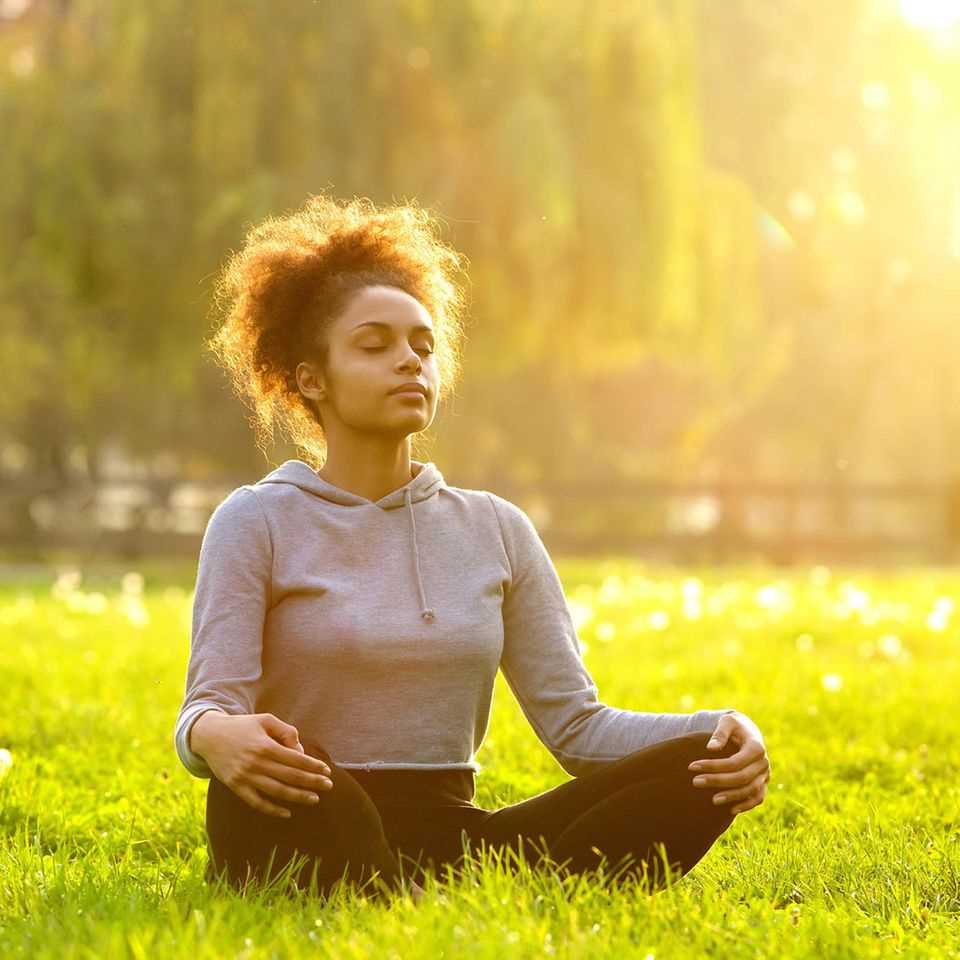 3 misunderstandings about meditation - and how it really is: Woman meditates outside on a meadow.