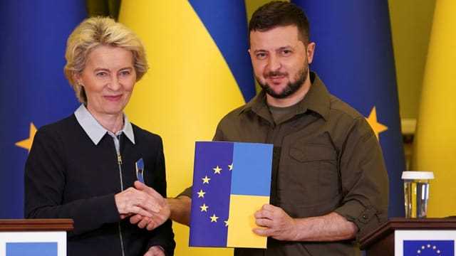 Von der Leyen und Selsnski halten ein Dokument mit der EU- und der Ukrainischen Flagge in den Händen.