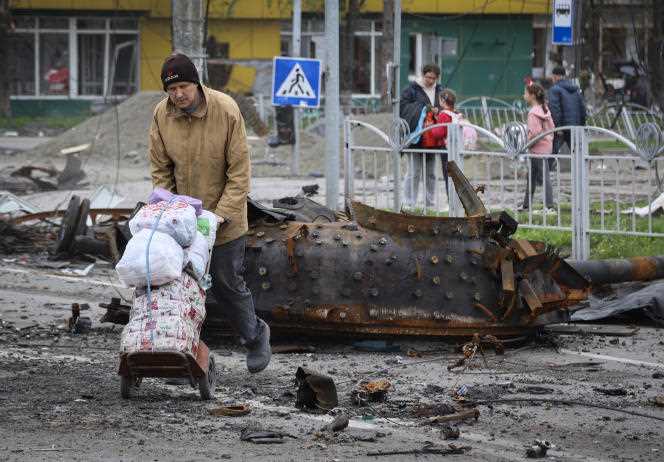 People walk near a damaged military vehicle in an area controlled by Russian-backed separatist forces, in Mariupol, Ukraine, April 23, 2022.