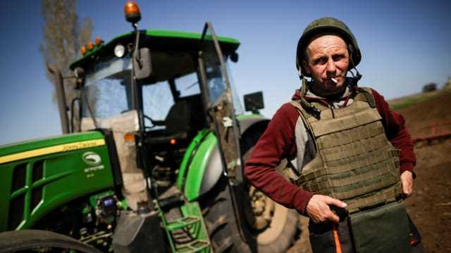Ein ukrainischer Bauer in militärischer Schutzausrüstung vor seinem Traktor.