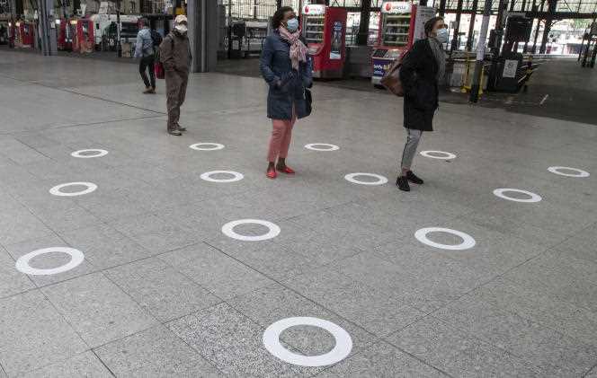 Masked people look at a train timetable board, outside markings on the ground intended to encourage physical distancing to protect against the spread of SARS-CoV-2, at Saint-Lazare train station in Paris on 5 May 2020.