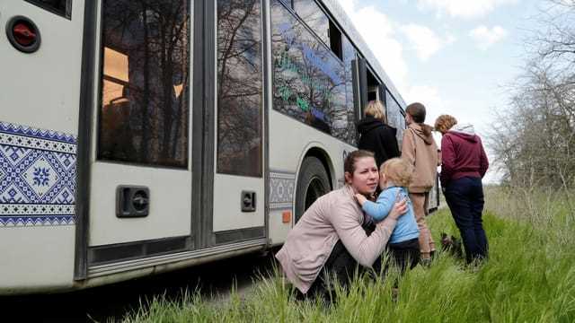 Eine Frau hält ein Kind neben einem Bus, während Zivilisten aus Mariupol, darunter Evakuierte aus dem Stahlwerk Azowstal, in einem Konvoi nach Saporischschja fahren.