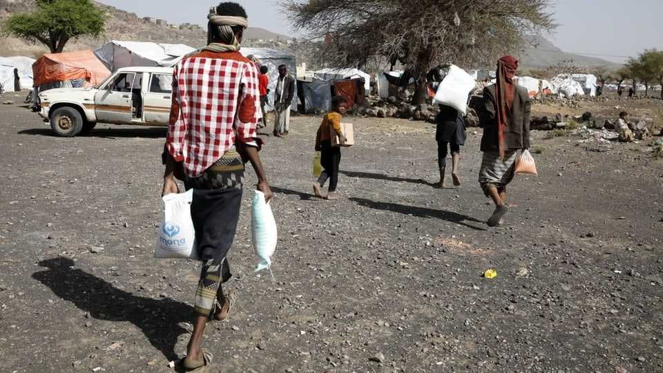 Men carry sacks (flour/rice?) from relief organizations, tents in the back.