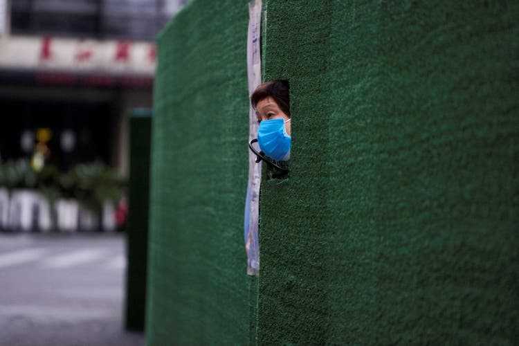 A resident looks through a barrier in her apartment block in Shanghai.  Food is served through the hatches.