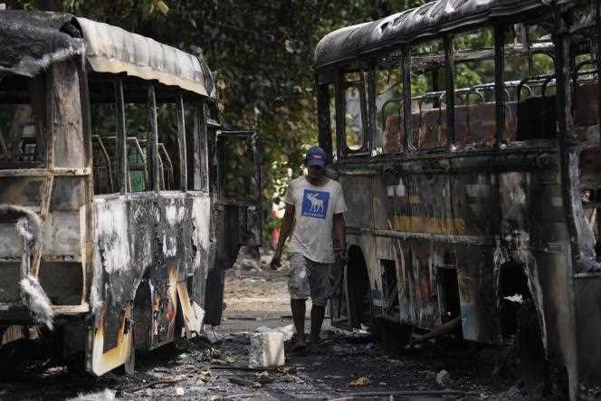 A Sri Lankan scrap picker searches for recyclable items near buses that were burned during clashes between government supporters and anti-government protesters, in Colombo, Sri Lanka, May 11, 2022.