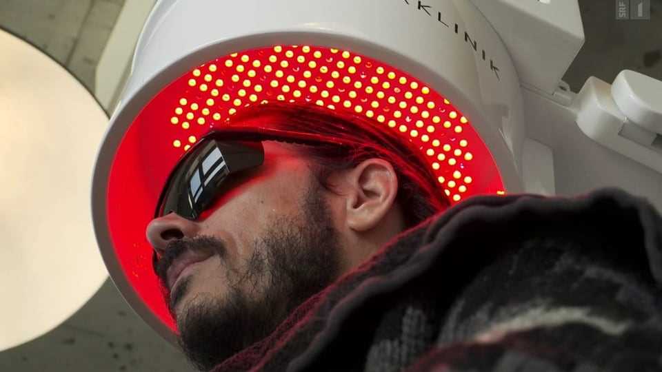 Man with glasses under a red glowing hood.