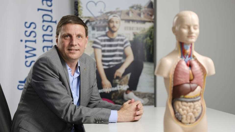 Middle-aged man posing for the camera while seated.  On the table a medicine doll visualizing the organs.