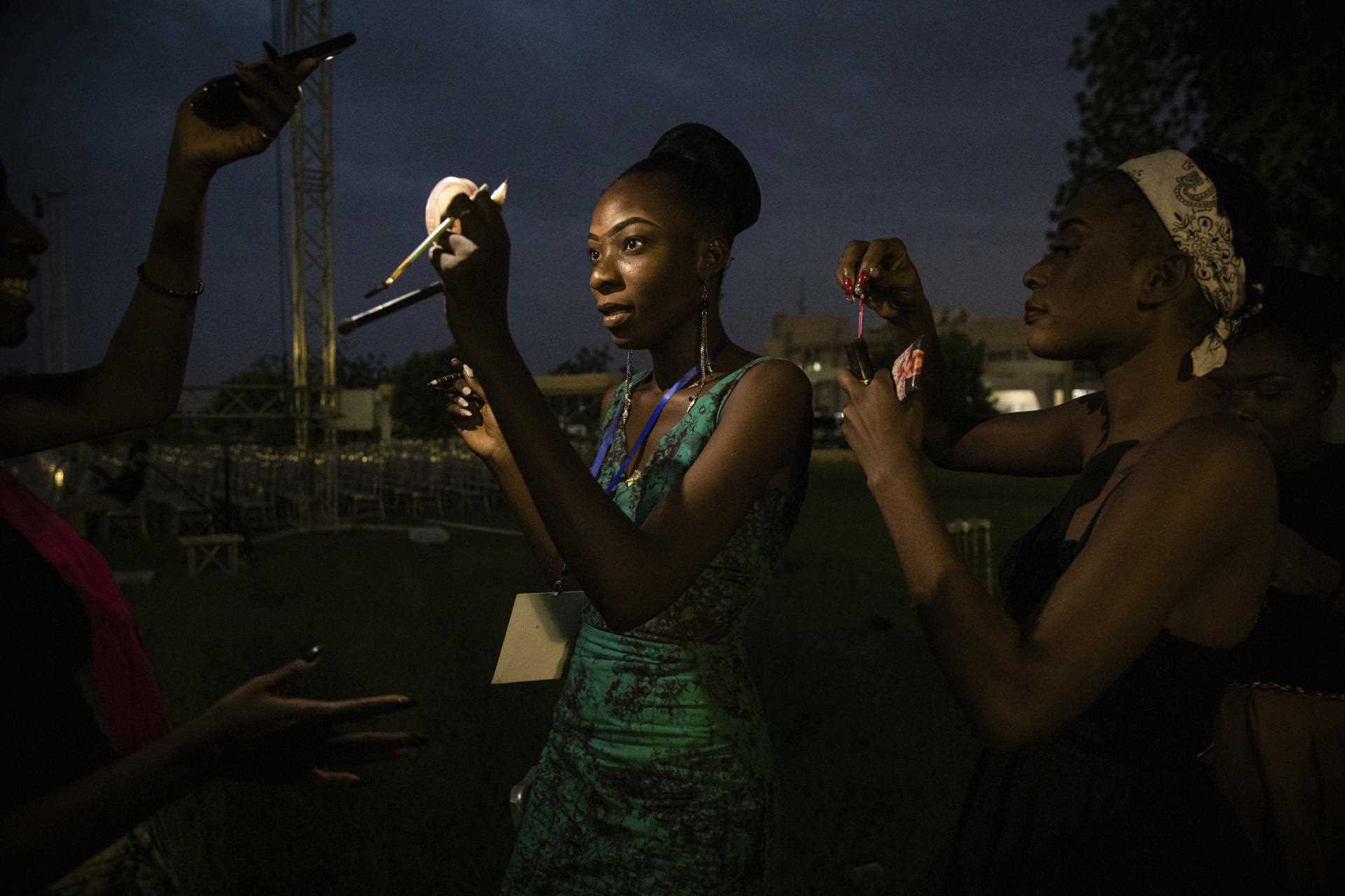 Teams use their phone lights during a power outage to apply makeup before the parade, Friday, May 13, 2022 in Ouagadougou, Burkina Faso. 