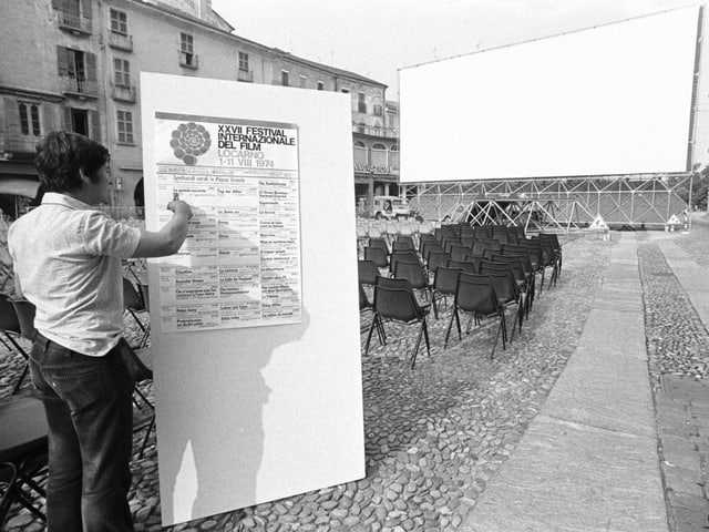 A man hangs up the festival program.  The canvas can be seen in the background.