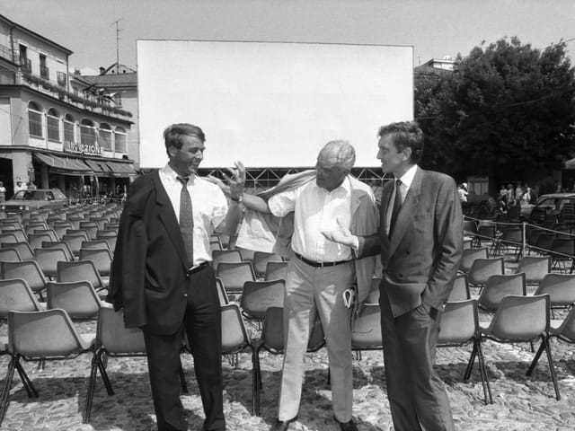 Three men stand in front of a blank canvas.