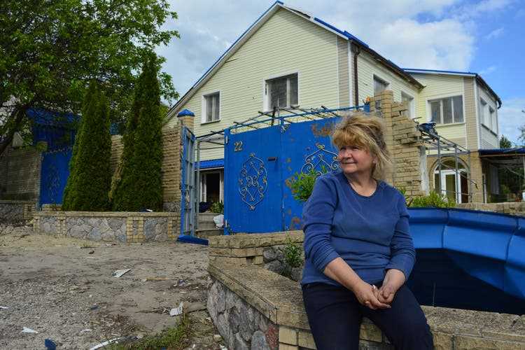 Ljuba sits on the wall in front of her damaged house in Wilchiwka.