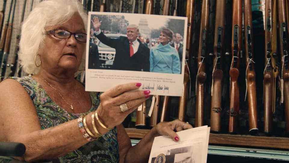 Gun store owner Linda Vernon holds picture of Donald and Melania Trump in front of gun wall 