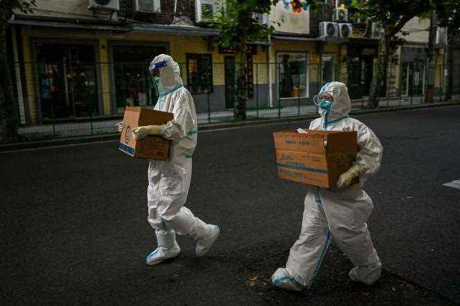 Health workers wearing protective gear walk on a street next to a residential area under lockdown in Shanghai's Xuhui district on June 8, 2022. 